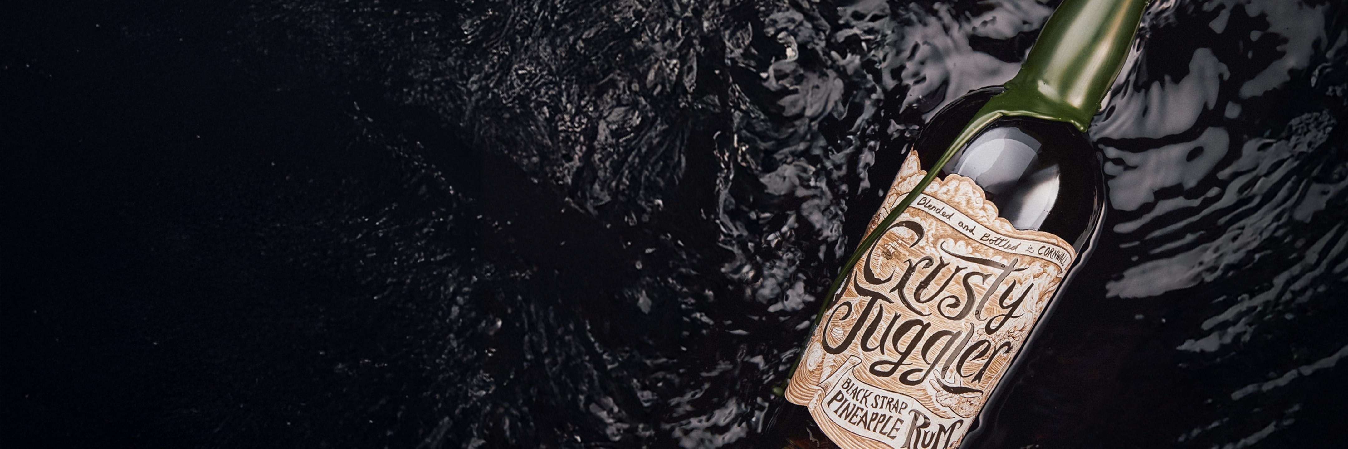 A bottle labeled Gutsy Jugglers with decorative text floats on dark, rippling water, its green cap and detailed label contrasting against the black background.