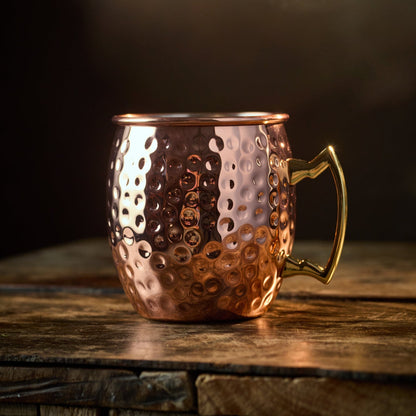A large Copper Mule Mug, featuring a textured copper-effect finish and a golden handle, sits on a rustic wooden table against a black background with warm lighting.
